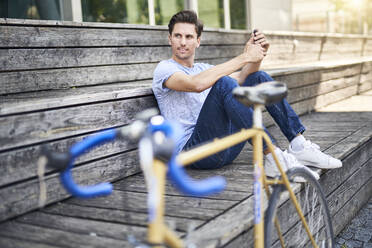 Porträt eines Mannes mit Rennrad auf einer Bank sitzend und sich ausruhend - PNEF01812