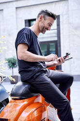 Älterer Mann, der ein Smartphone benutzt und auf einem Motorroller sitzt - PNEF01830
