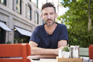Lächelnder reifer Mann mit Smartphone sitzt in einem Straßencafé - PNEF01838