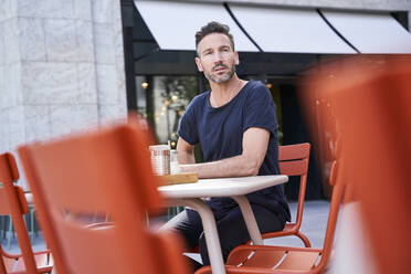 Lächelnder reifer Mann, der in einem Straßencafé sitzt und sich umschaut - PNEF01839