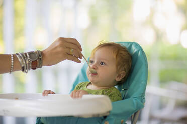 Caucasian mother feeding baby in high chair - BLEF13752