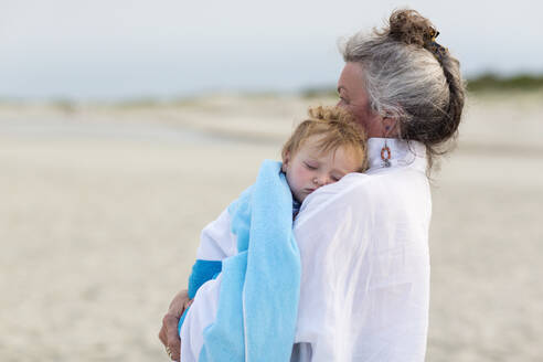Kaukasische Frau trägt Enkel am Strand - BLEF13755