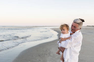 Caucasian woman carrying grandson on beach - BLEF13765