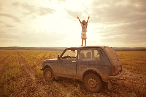 Mari Junge steht auf dem Autodach in einem ländlichen Feld - BLEF13819