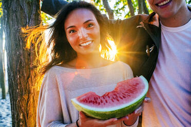 Kaukasisches Paar isst Wassermelone bei Sonnenuntergang - BLEF13844