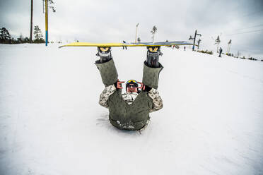 Caucasian snowboarder laying in snow with legs raised - BLEF13852