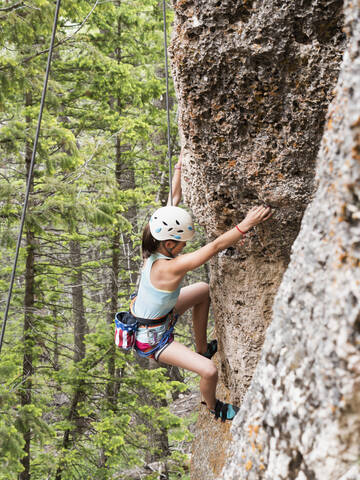 Gemischtrassiges Mädchen klettert auf steilen Felsen, lizenzfreies Stockfoto