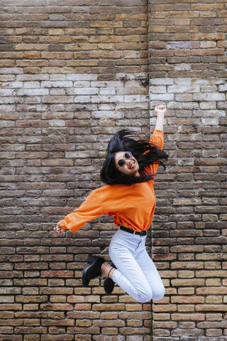 Asiatische Frau springt, Backsteinmauer im Hintergrund, lizenzfreies Stockfoto