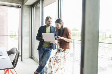 Young businesswoman and businessman using laptop at the window in office - UUF18499