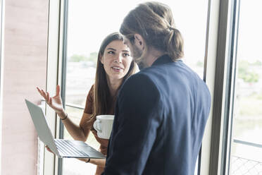 Young businesswoman and businessman using laptop at the window in office - UUF18501