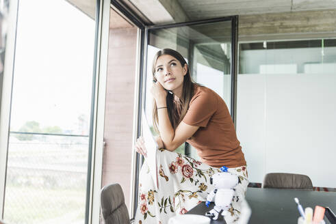 Junge Geschäftsfrau sitzt am Schreibtisch im Büro und denkt nach - UUF18505