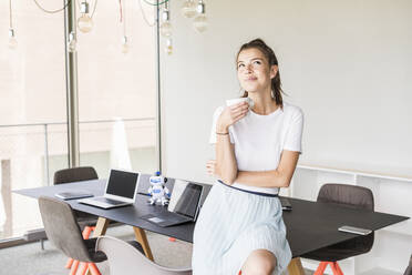 Young businesswoman having coffee break in office looking up - UUF18522