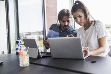 Young man and woman working together on laptop at desk in office - UUF18542