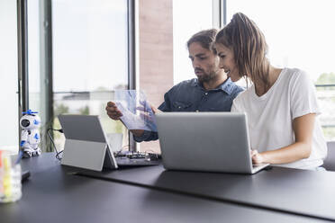 Young man and woman working together at desk in office - UUF18543