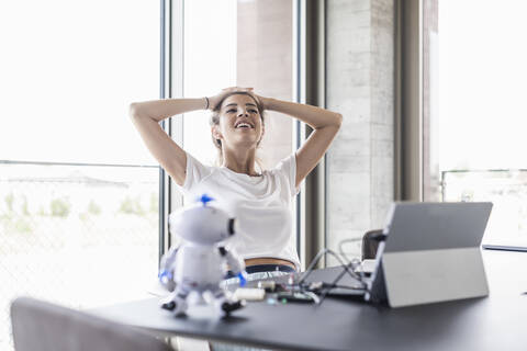 Lächelnde junge Frau sitzt am Schreibtisch im Büro und macht eine Pause, lizenzfreies Stockfoto