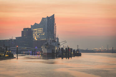 Elbphilharmonie by Elbe River against sky in city during sunrise at Hamburg, Germany - KEB01272