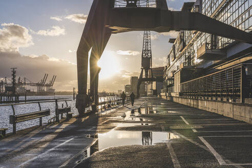 Diminishing perspective of wet footpath by Elbe River during sunset, Hamburg, Germany - KEBF01282
