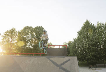 Young man riding BMX bike at skatepark at sunset - AHSF00744