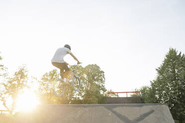 Young man riding BMX bike at skatepark at sunset - AHSF00746