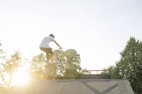 Junger Mann fährt BMX-Rad im Skatepark bei Sonnenuntergang - AHSF00746