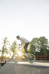 Young man riding BMX bike at skatepark at sunset - AHSF00747