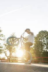 Young man riding BMX bike at skatepark at sunset - AHSF00748