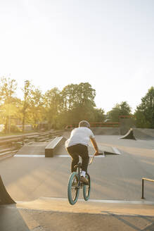 Rückansicht eines jungen Mannes auf einem BMX-Rad im Skatepark bei Sonnenuntergang - AHSF00751