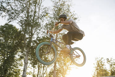 Young man jumping with BMX bike at sunset - AHSF00752