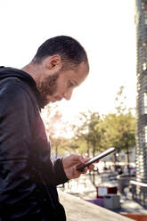 Mann benutzt Mobiltelefon bei Sonnenuntergang in der Stadt, Barcelona, Spanien - GEMF03106
