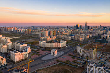 Luftaufnahme des Triumphbogens, Nur Sultan, Kasachstan bei Sonnenaufgang. Sie zeigt den Bau weiterer passender Hochhäuser um den Triumphbogen. - AAEF01366