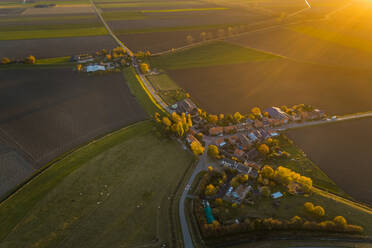Luftaufnahme eines kleinen Dorfes, das von landwirtschaftlichen Flächen umgeben ist, während eines malerischen Sonnenuntergangs, Niederlande. - AAEF01419