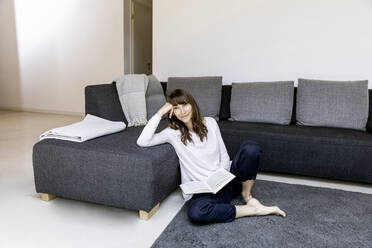 Porträt einer entspannten Frau mit Buch im Wohnzimmer - FMKF05833