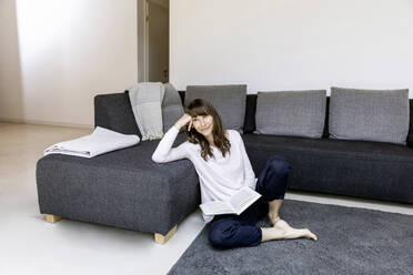 Portrait of relaxed woman with book in living room - FMKF05833