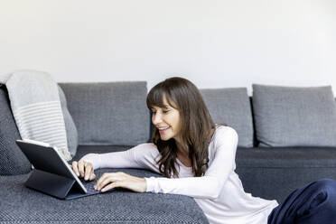 Relaxed woman using tablet in living room at home - FMKF05835