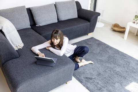Entspannte Frau mit Tablet im Wohnzimmer zu Hause, lizenzfreies Stockfoto