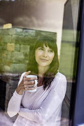 Porträt einer lächelnden Frau, die eine Tasse Kaffee zu Hause hält - FMKF05840