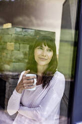 Portrait of smiling woman holding cup of coffee at home - FMKF05840