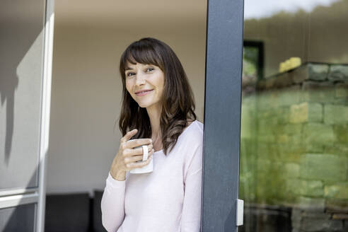 Porträt einer lächelnden Frau, die eine Tasse Kaffee zu Hause hält - FMKF05841