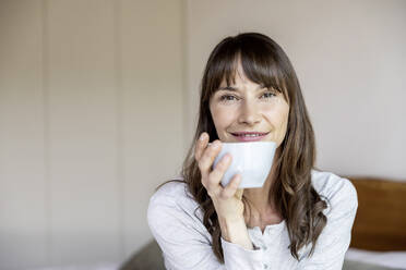 Porträt einer entspannten Frau, die eine Tasse Kaffee zu Hause hält - FMKF05849