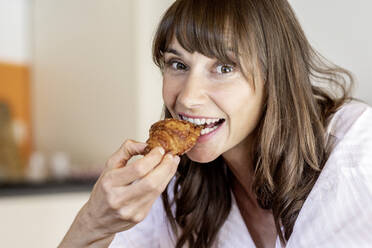 Porträt einer glücklichen Frau, die ein Croissant isst - FMKF05862
