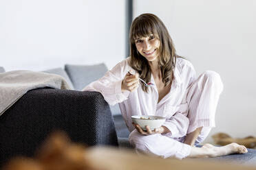 Porträt einer lächelnden Frau beim Frühstück auf der Couch zu Hause - FMKF05864