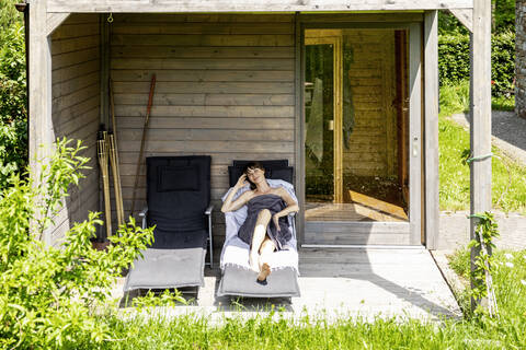 Frau entspannt sich auf einer Liege außerhalb der Sauna, lizenzfreies Stockfoto