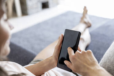 Nahaufnahme einer entspannten Frau, die zu Hause auf der Couch ihr Smartphone benutzt - FMKF05879