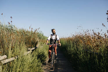 Well dressed man with his bike on a wooden walkway in the countryside after work - JRFF03569