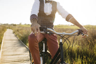 Well dressed man with his bike on a wooden walkway in the countryside after work - JRFF03582