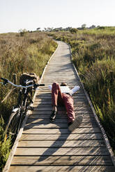 Gut gekleideter Mann mit Laptop auf einem Holzsteg in der Natur neben einem Fahrrad liegend - JRFF03604