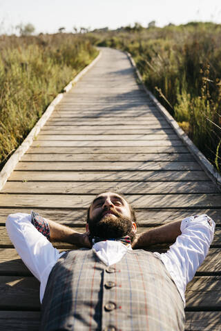 Gut gekleideter Mann auf einem Holzsteg in der Natur liegend, lizenzfreies Stockfoto