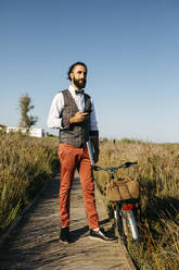 Well dressed man with his bike on a wooden walkway in the countryside having a break - JRFF03612