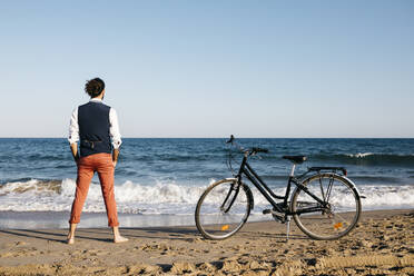 Gut gekleideter Mann mit seinem Fahrrad am Strand stehend - JRFF03622