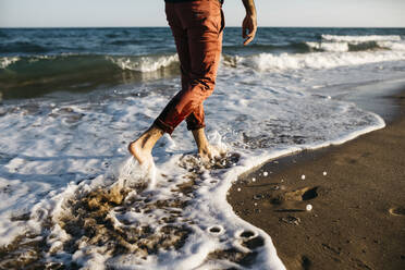 Rückansicht eines Mannes mit orangefarbener Hose, der an einem Strand spazieren geht - JRFF03625